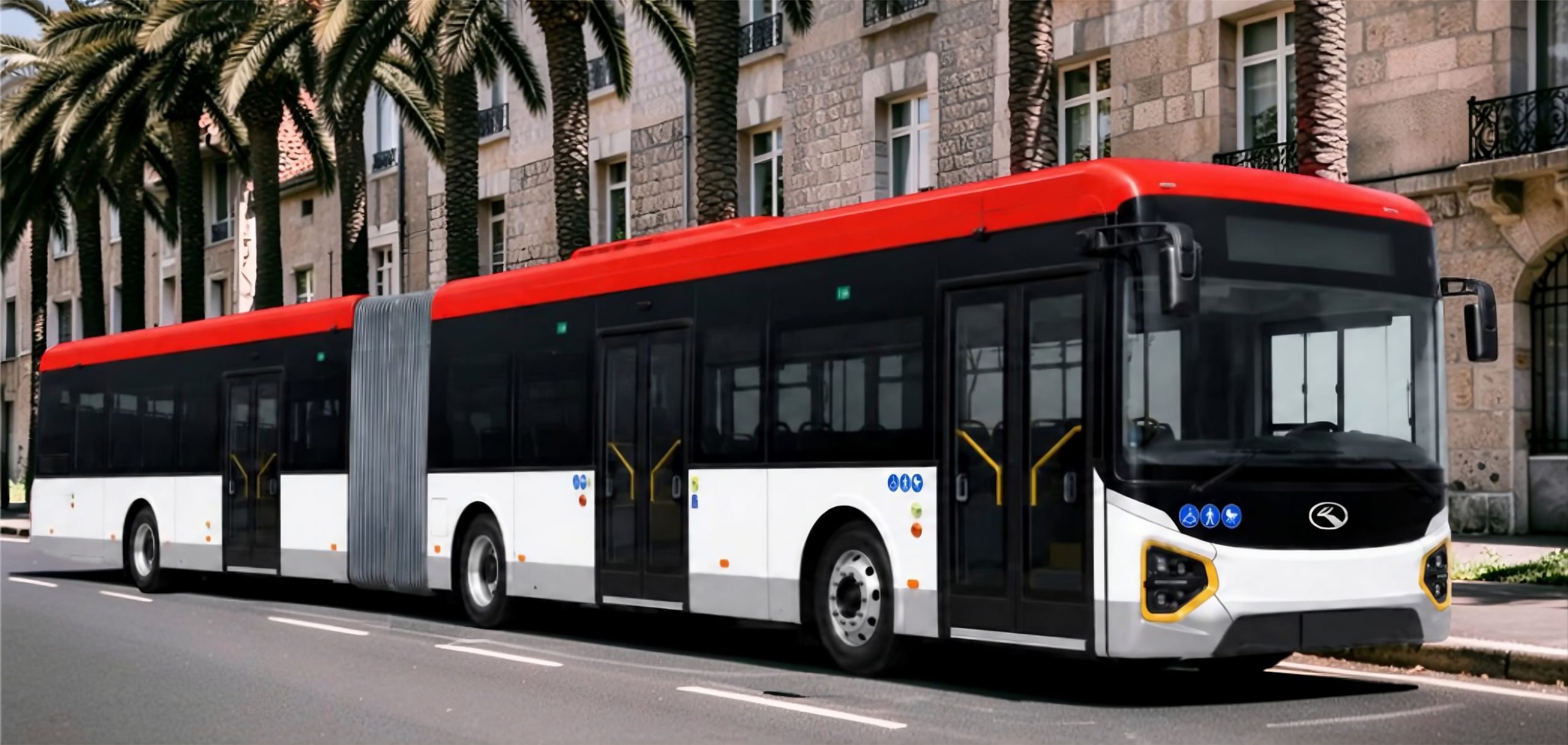 autobus electrico articulado en una calle con palmeras y edificios